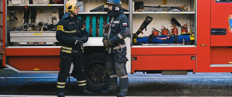 Zwei Feuerwehrleute in Einsatzkleidung am geöffneten Löschfahrzeug