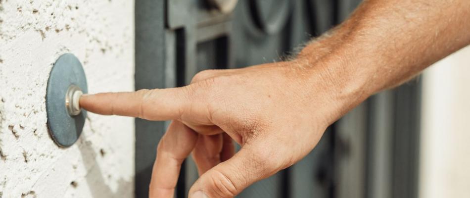 Hand drückt den Klingeltaster neben einer Haustür