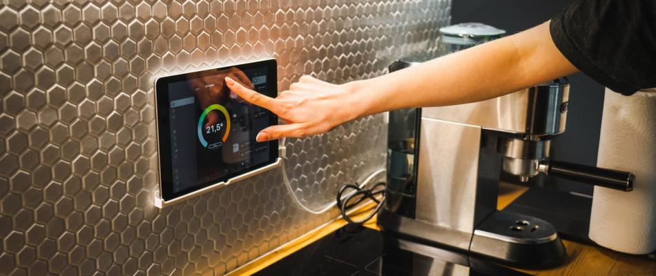 Hand bedient ein Touch-Bedienfeld der Gebäudeautomation an der Küchenwand