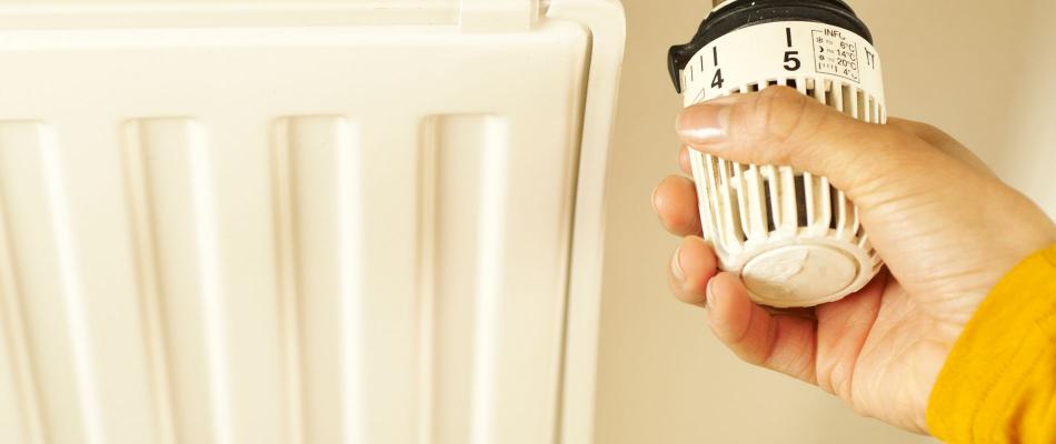 Hand dreht am Thermostat eines Heizkörpers