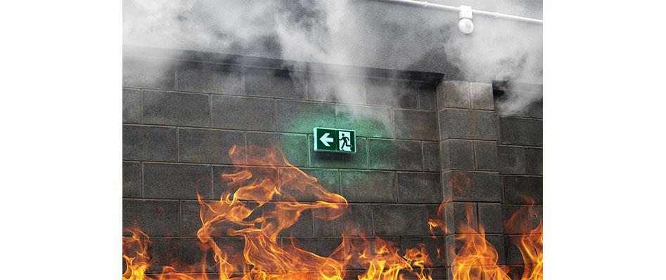 Flammen und Rauch vor einer Betonwand mit beleuchtetem Notausgangsschild