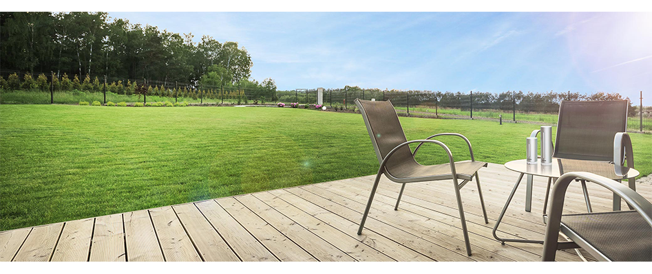 Holzterrasse mit Gartenstühlen und Blick über einen gepflegten Rasen bei Sonnenschein